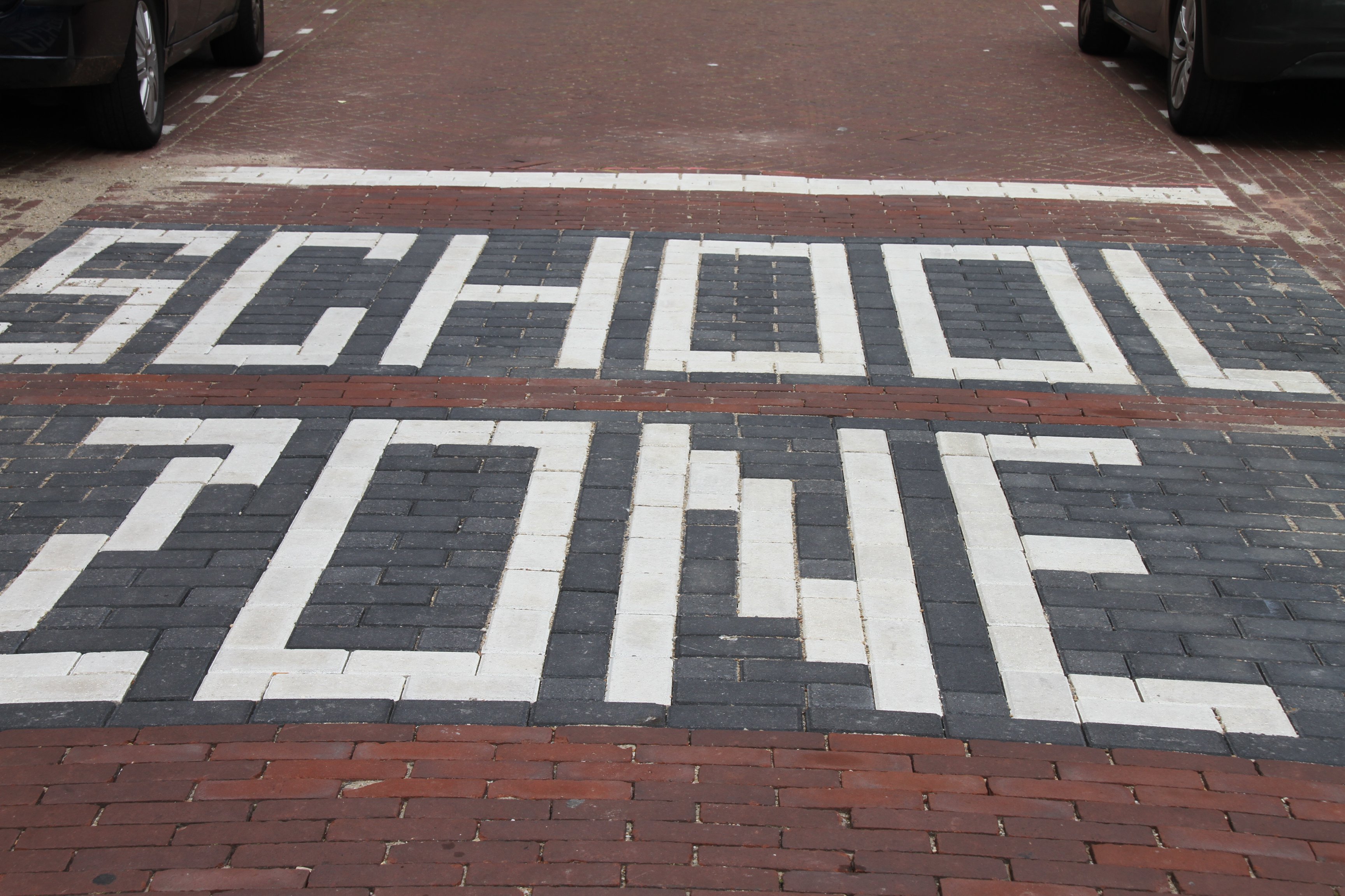 Straatstenen vormen de tekst: school zone